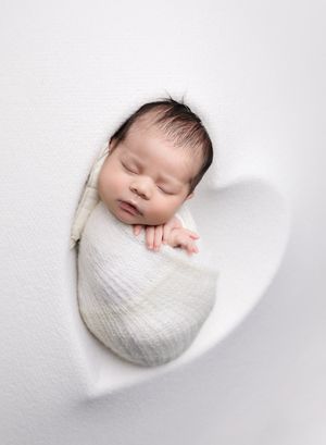 Studio newborn photography portrait of sleeping baby wrapped in white on heart shaped backdrop photographed by Valerie Kay Photography Austi