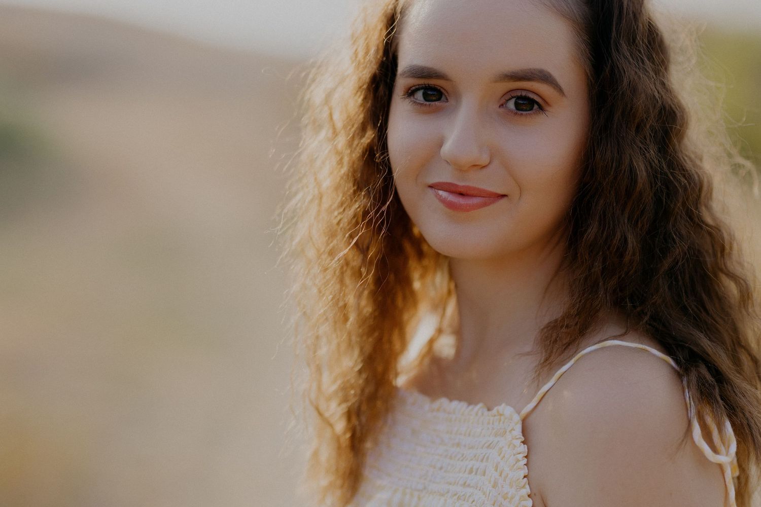 A person with curly brown hair poses outdoors in golden sunlight during a portrait photoshoot.