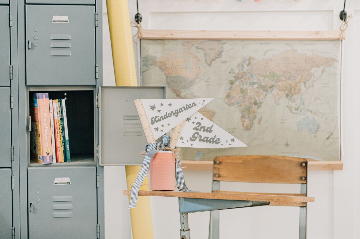 Vintage classroom corner with gray metal lockers, a world map, wooden desk, and a pennant banner reading Kindergarten 2nd Grade.