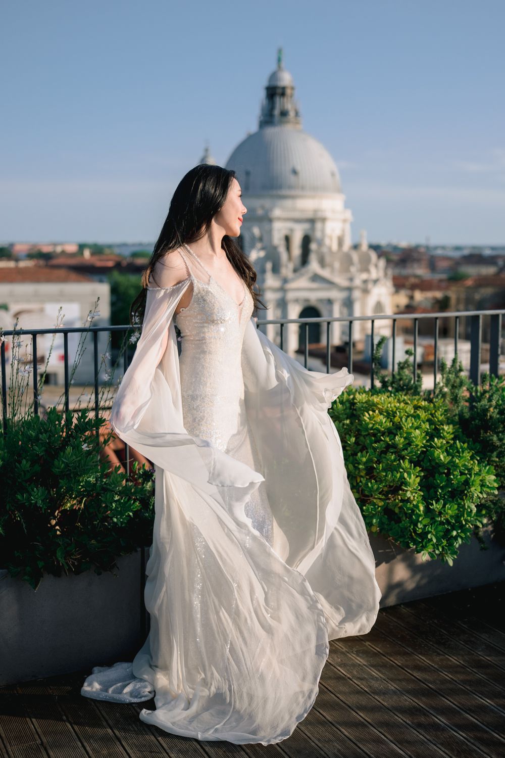Bride in flowing white gown on Venice rooftop with Santa Maria della Salute dome backdrop.
