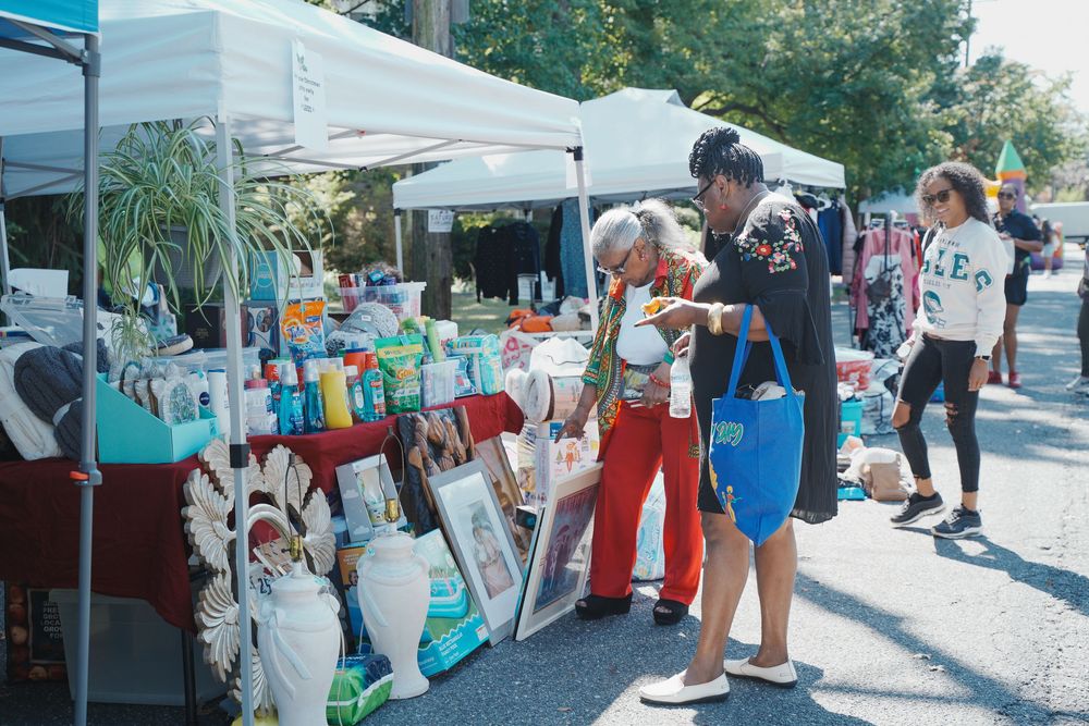 Two women browse items at an outdoor vendor booth filled with various goods for sale.
