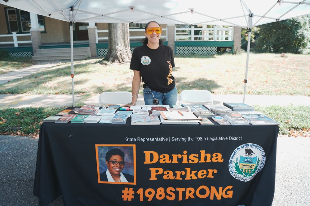A person stands behind a table with a Darisha Parker 198Strong campaign banner at an outdoor event.