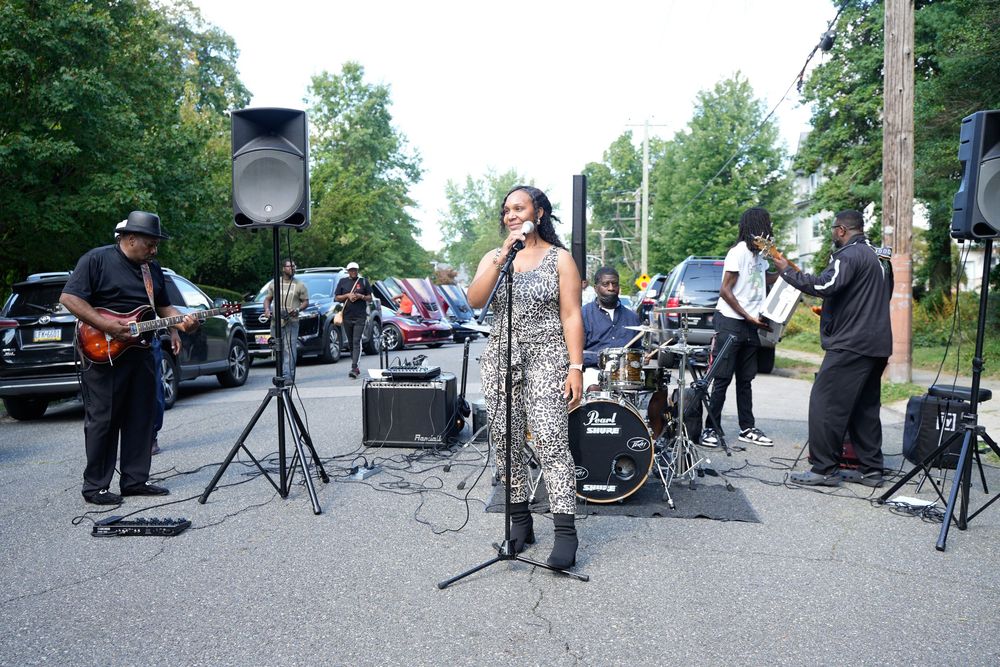 Live band performing outdoors on a street, featuring a female vocalist in a sequined outfit.