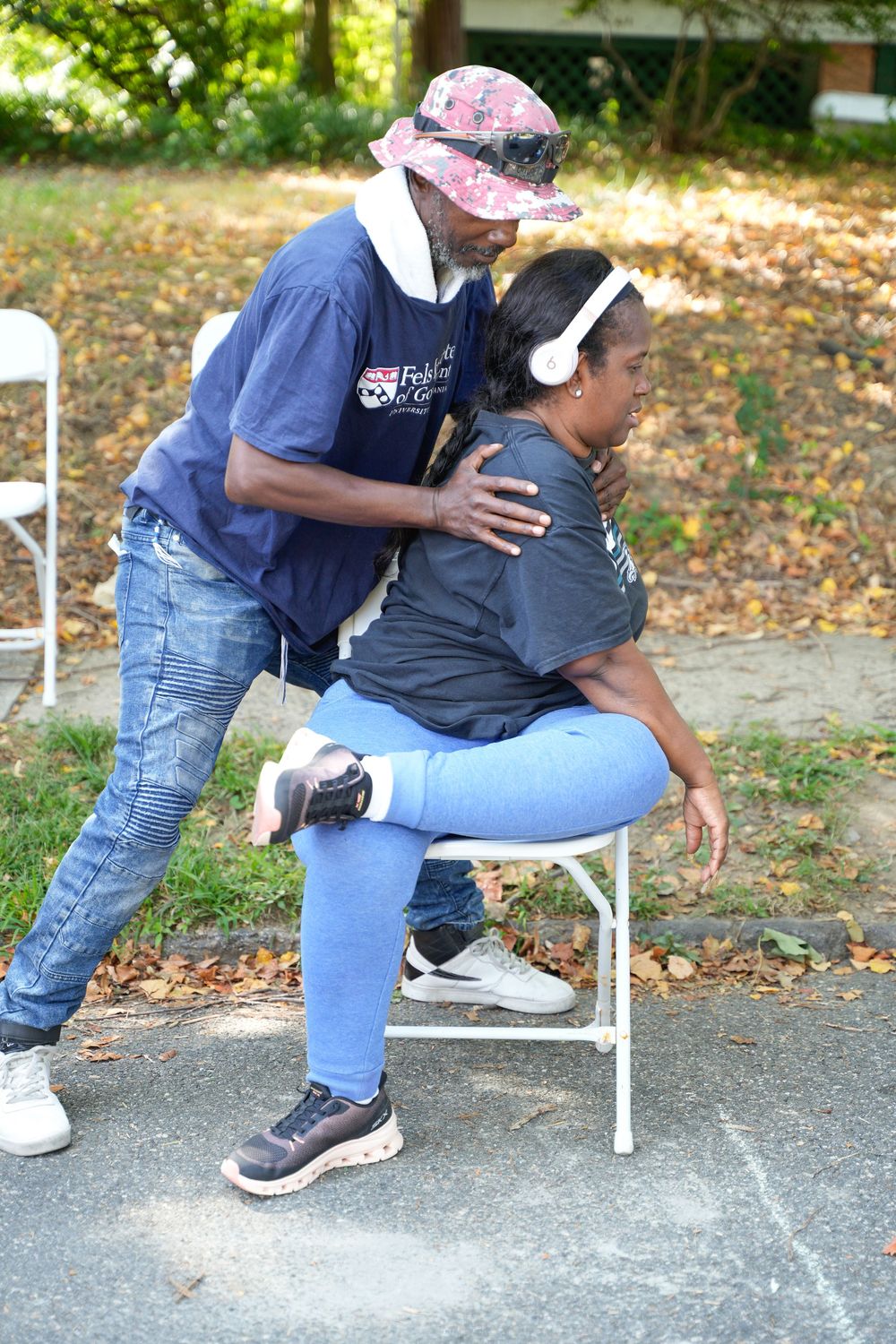 A man gives an outdoor chair massage to a woman wearing headphones at a community health event.