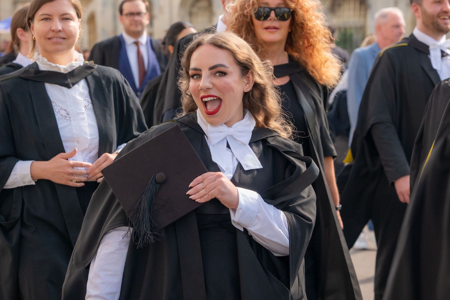 Joyful graduate in black academic gown and white collar holds diploma at university graduation ceremony.