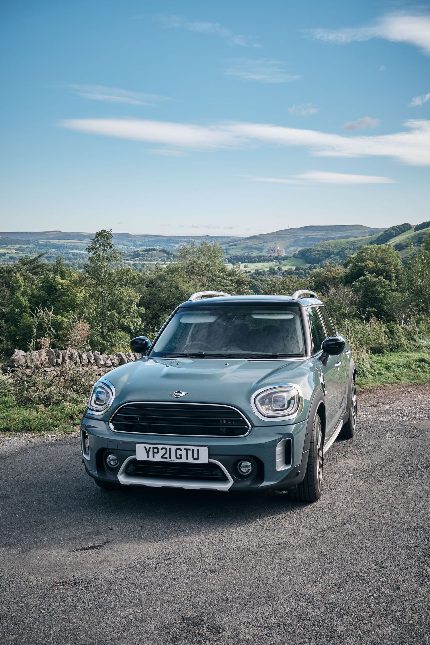 A green MINI Countryman SUV parked on a rural road with rolling hills and blue sky in the Yorkshire countryside.