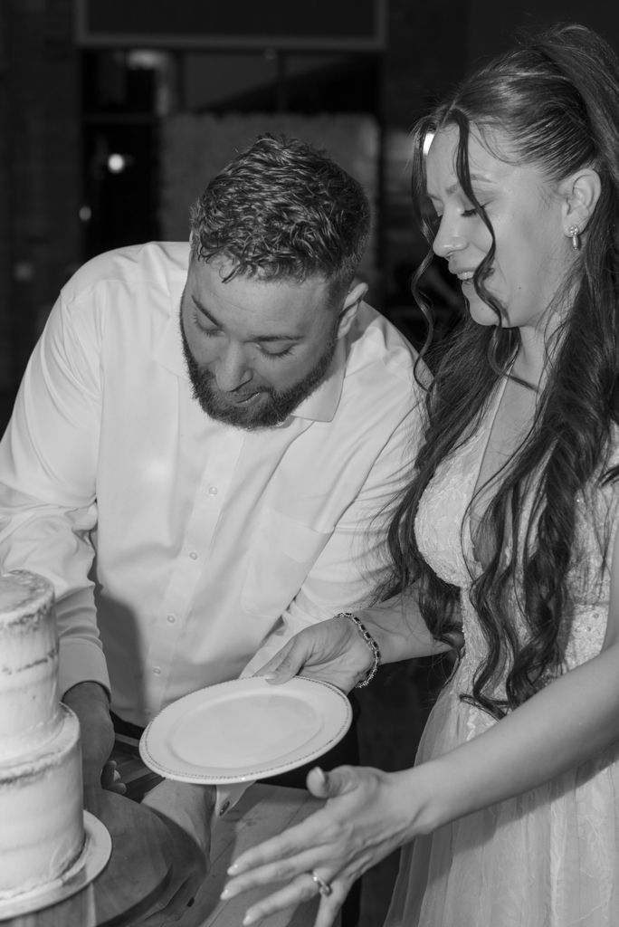 Black and white photo of bride and groom cutting their wedding cake together at reception.