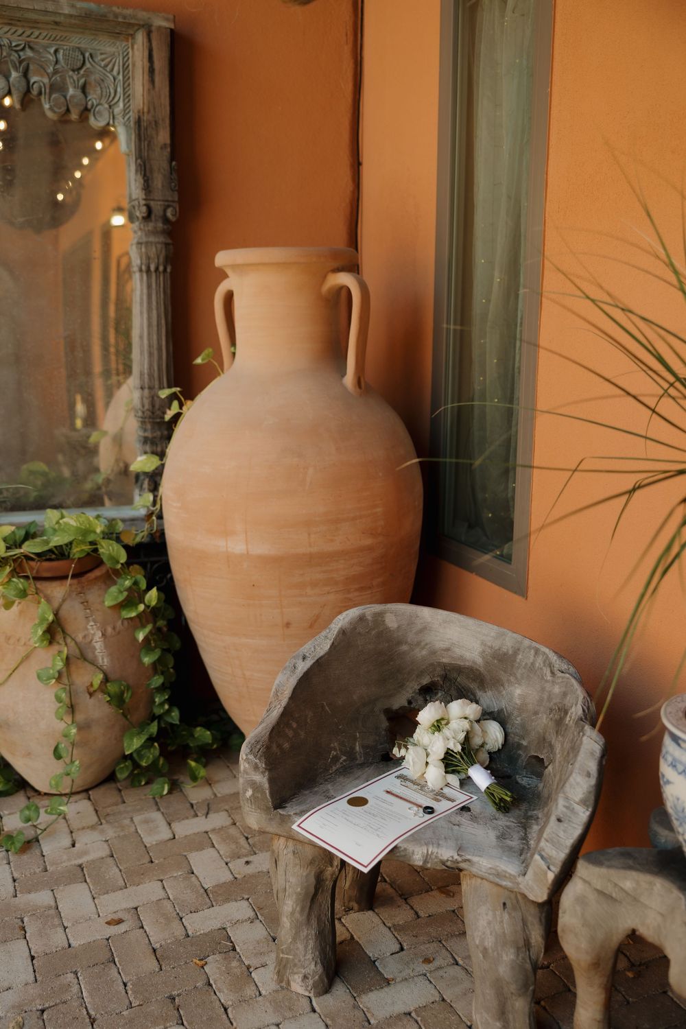 White wedding bouquet resting on rustic stone chair beside large terracotta amphora vase.