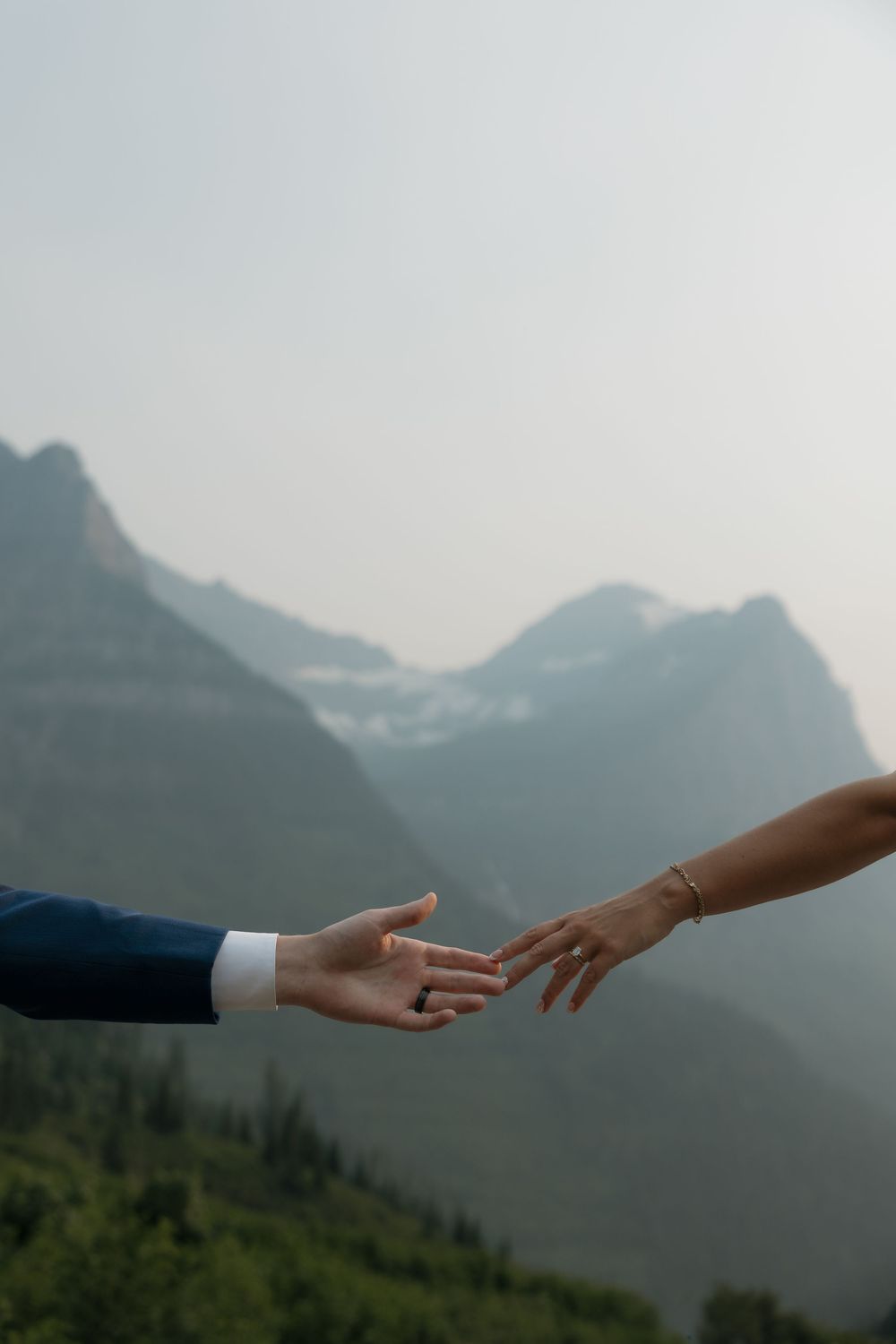 Two hands reaching toward each other with misty mountain landscape in background, wedding couple moment.