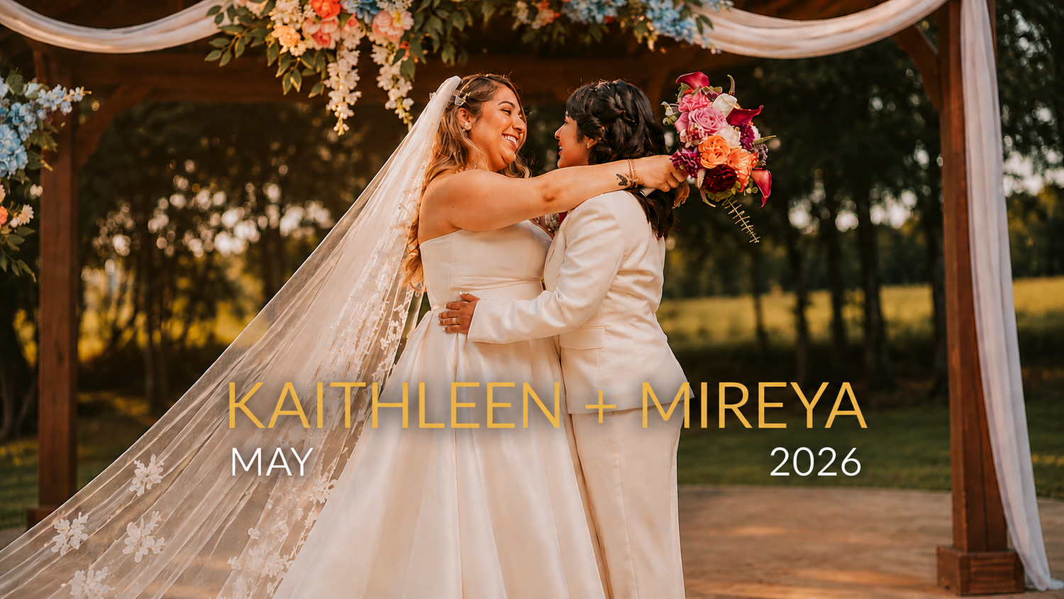 Kaithleen and Mireya share a romantic kiss under a floral arch at their outdoor wedding in May 2026.