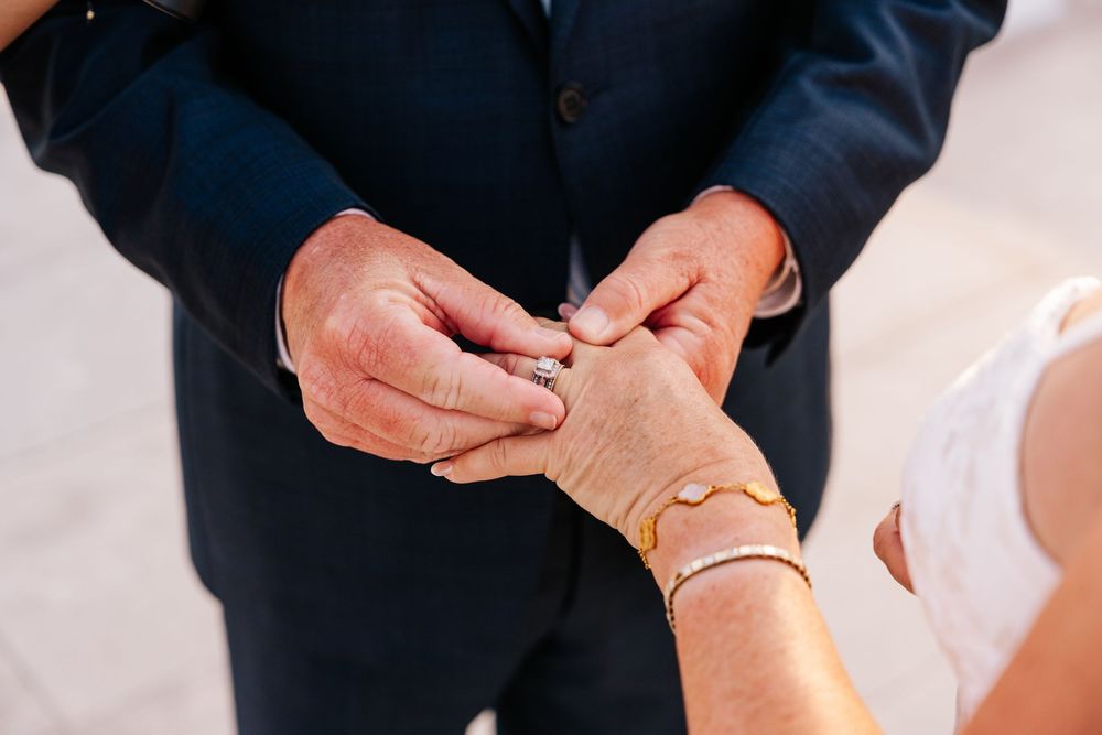 Groom placing a wedding ring on bride's finger during ceremony, bride wearing gold bracelet.