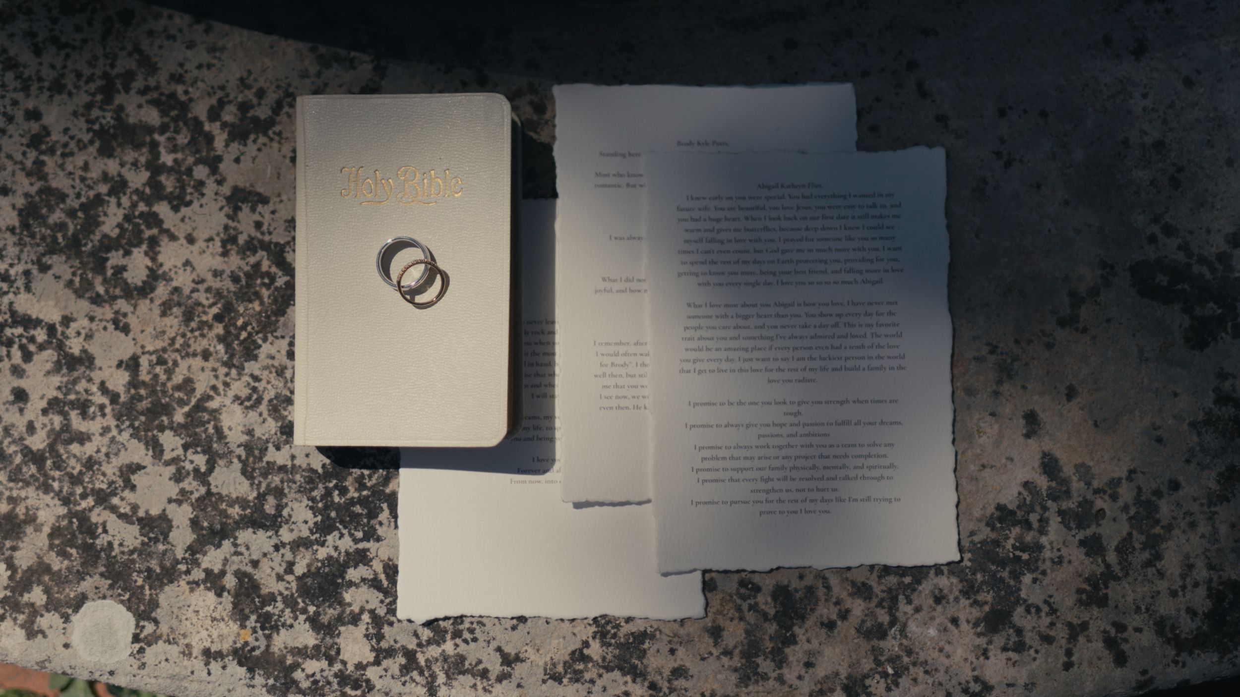 A wedding booklet with two interlocked rings on the cover beside printed ceremony papers on a granite surface.