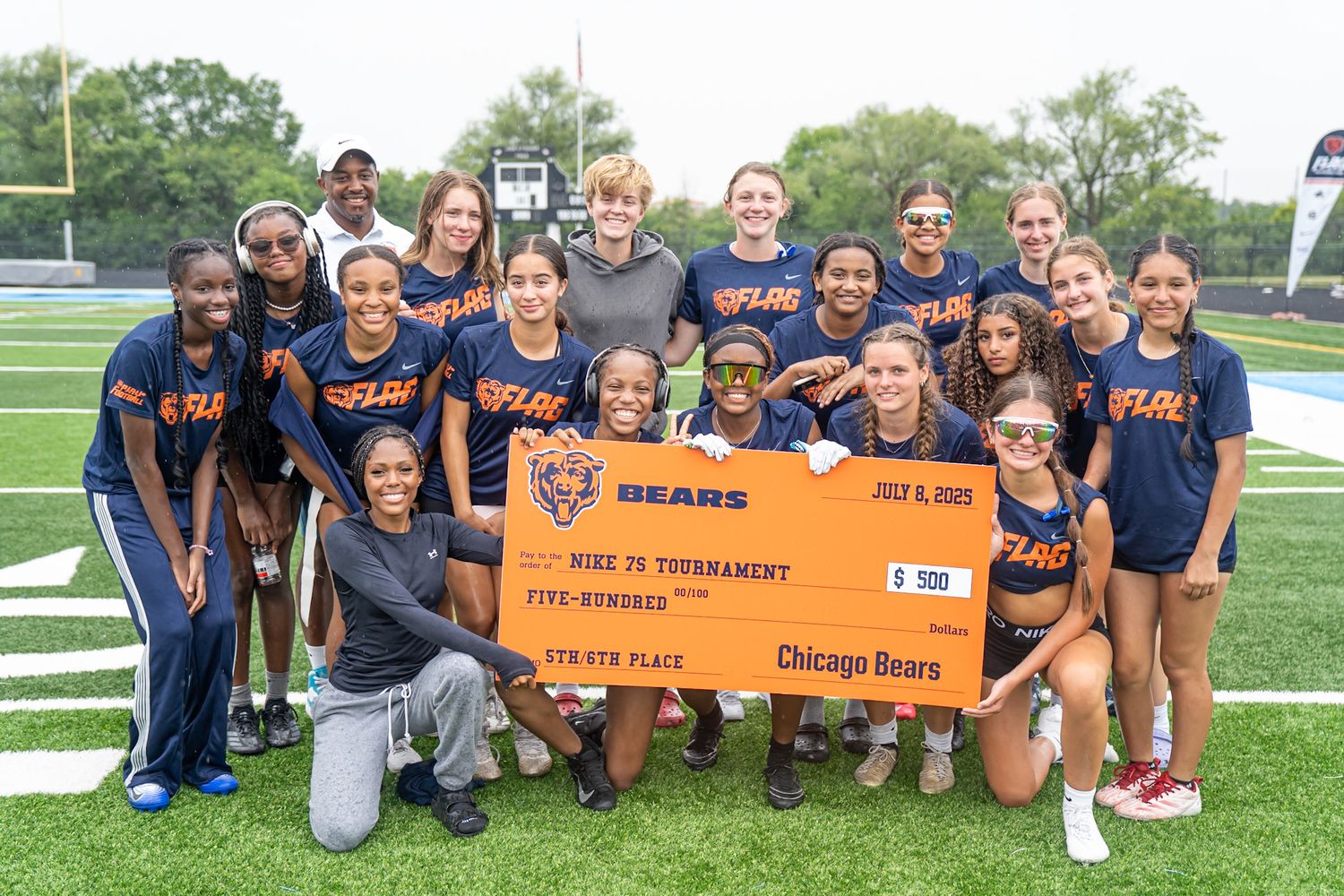 Chicago Bears youth flag football team poses with a $500 tournament check on a green turf field.