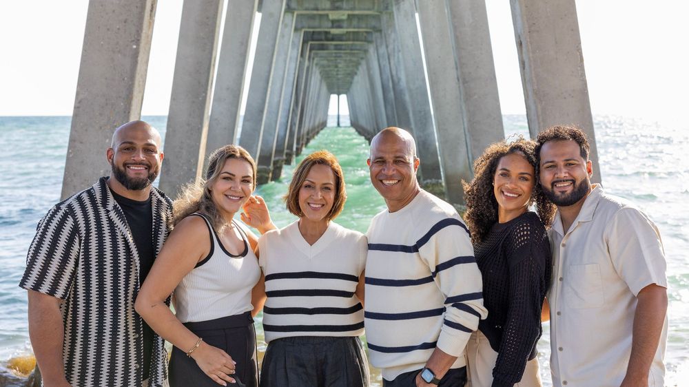 Family group photo under a pier with ocean view wearing coordinated striped and white outfits.