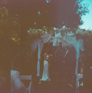 Outdoor wedding ceremony under a floral chuppa with draped white fabric at dusk.