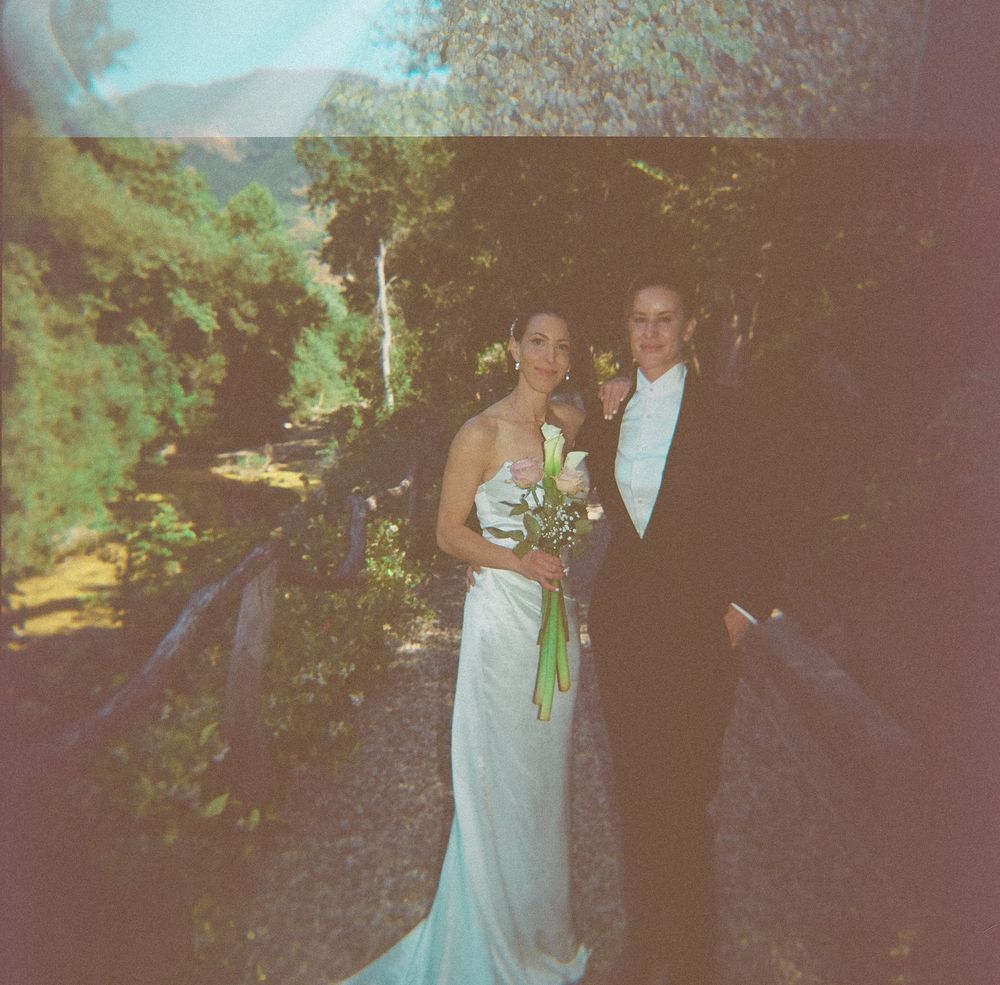 Bride in white gown holding bouquet stands with groom in black tuxedo outdoors on their wedding day.