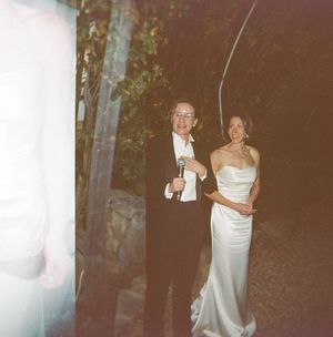 Couple in formal attire, bride in white strapless gown and partner in black suit, posing outdoors at night.