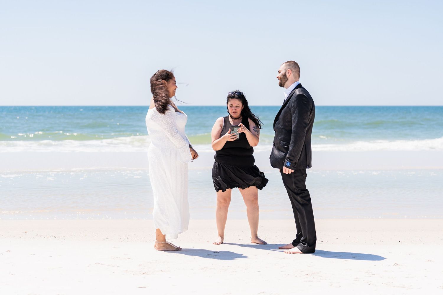 Couple exchanges vows with officiant on a sunny beach wedding ceremony by the ocean.