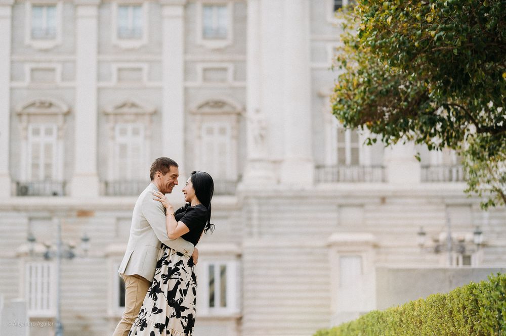Romantic couple embracing and gazing at each other in front of grand white palace facade.