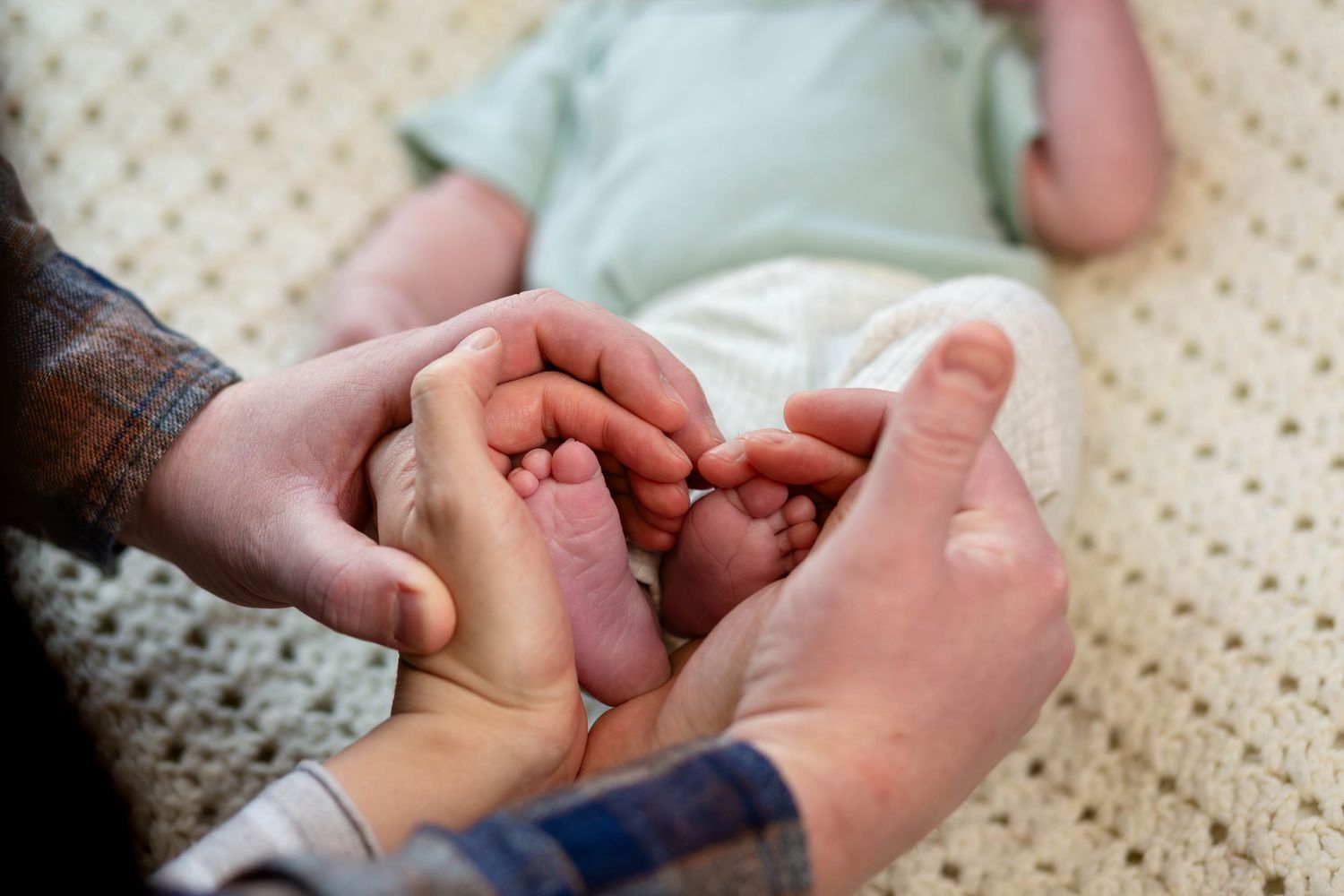 Two parents gently hold their newborn baby's tiny feet together in a tender and loving moment.