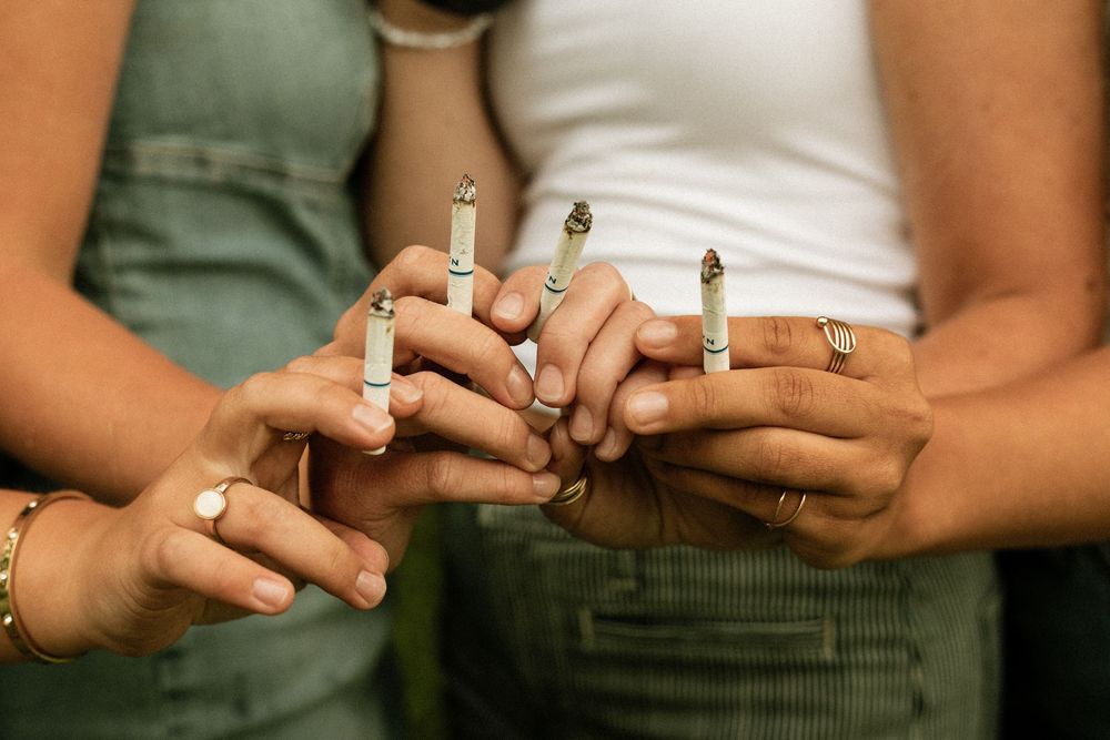 Close-up of three women holding cannabis joints together, wearing rings and bracelets outdoors.