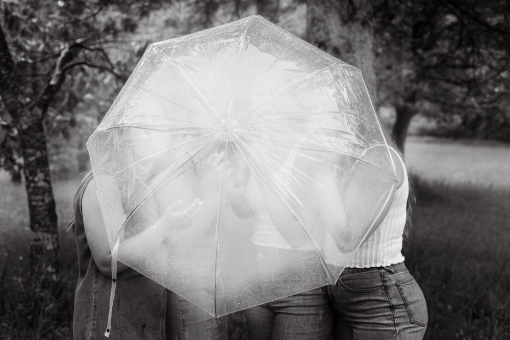 Couple sharing a romantic moment hidden behind a clear transparent umbrella in a black and white outdoor photo.