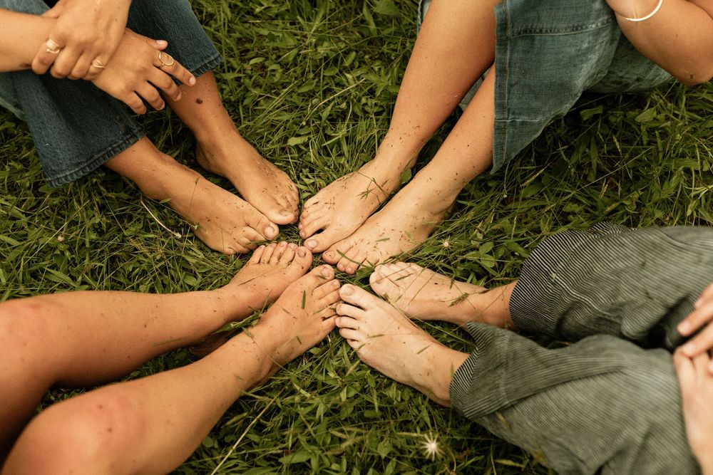 Group of people sitting in a circle on grass with bare feet touching in the center.