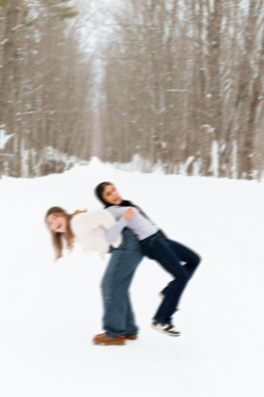 Two girls playing and laughing in snowy winter woods, one giving the other a piggyback ride.