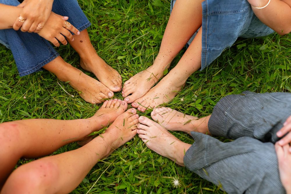 Group of people sitting in a circle on grass with bare feet touching in the center.