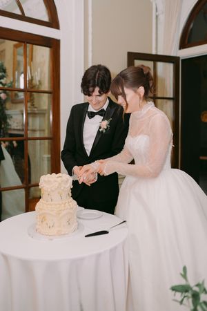 Bride and groom cutting a two-tier white wedding cake together at an elegant indoor reception venue.
