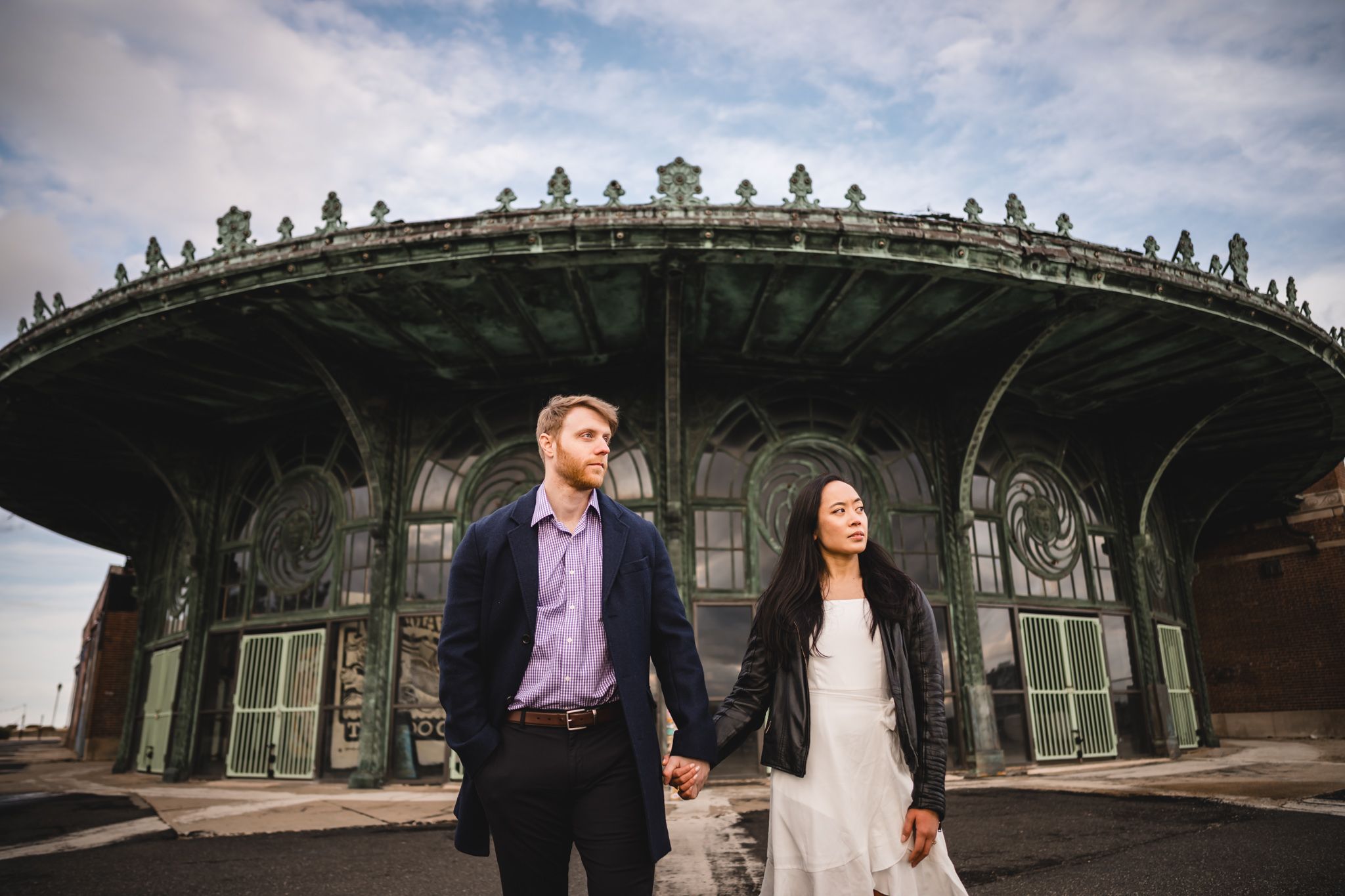 Couple holding hands in front of ornate green historic building under cloudy sky.