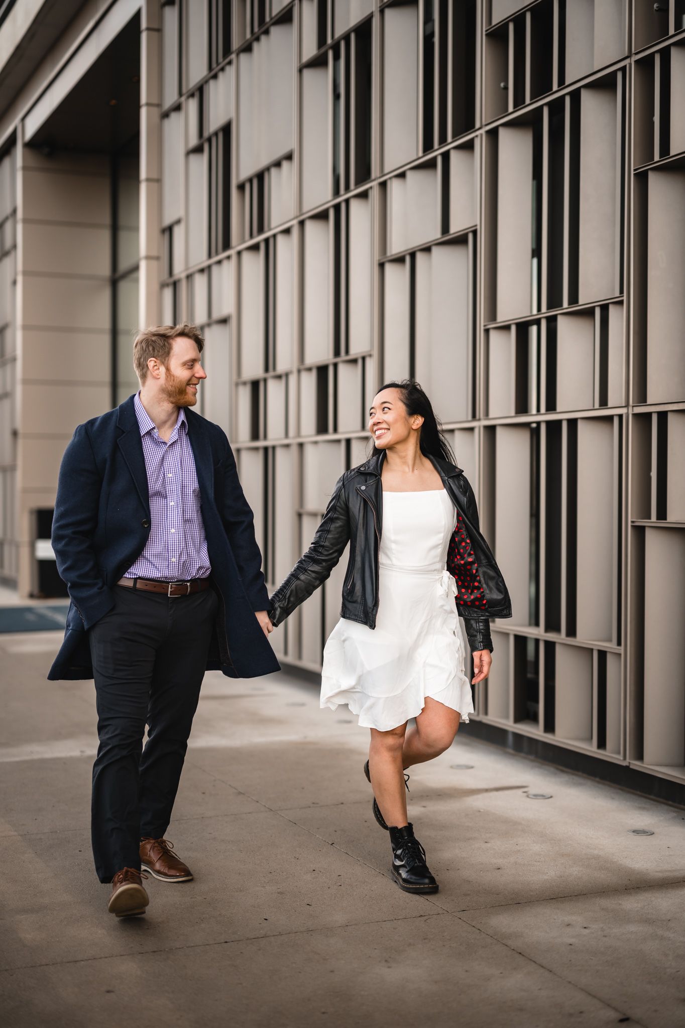 Happy couple holding hands and walking together outside a modern building in urban setting.