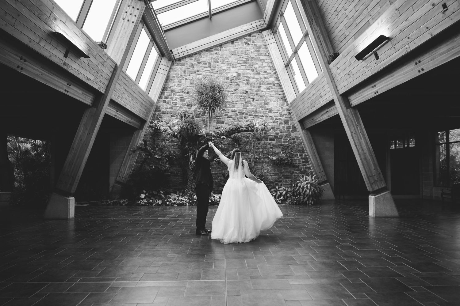 Bride and groom share a romantic moment under a white umbrella on a scenic overlook with forest and river views.