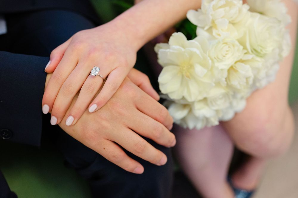 Bride and groom hands with diamond engagement ring and wedding bouquet of white roses closeup.