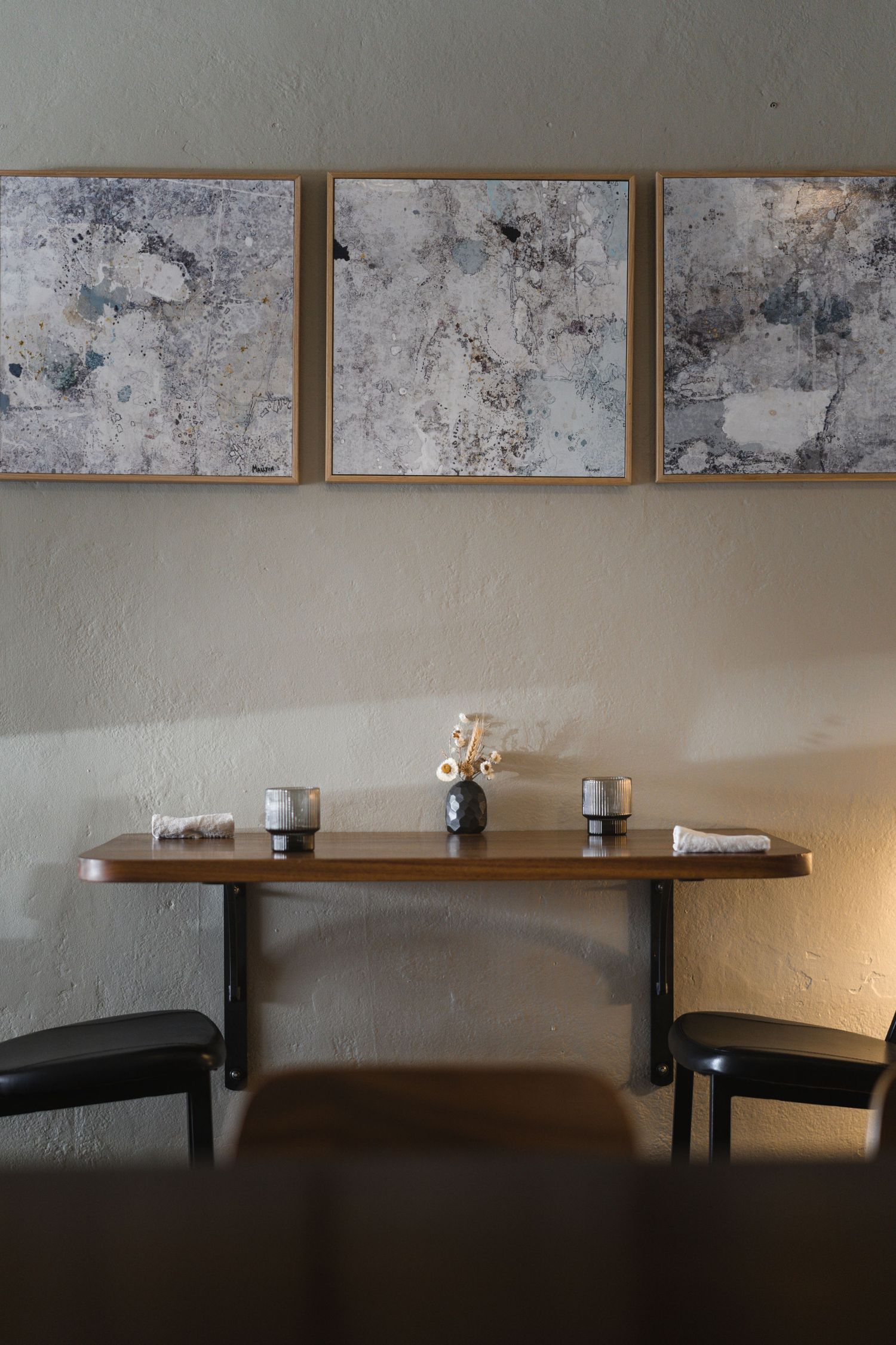 Three framed abstract artworks above a wooden wall-mounted table with ceramic vases in a cafe setting.

Surly Goat