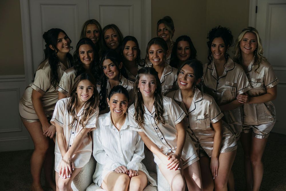 Bride in white robe poses with bridesmaids in matching champagne satin pajamas for a getting-ready photo in Chicago