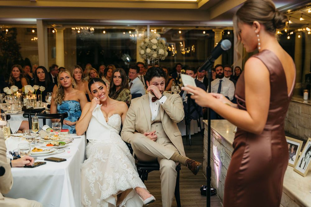 Bride and groom emotional during wedding reception speech, guests watching in background at elegant Meson Sabika venue in Naperville, IL
