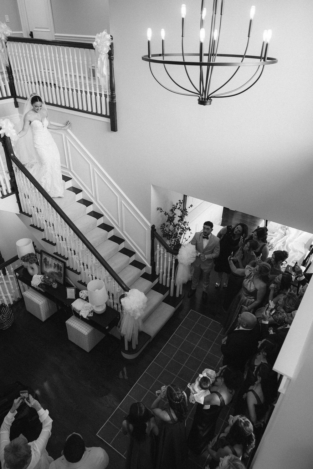 Black and white aerial view of a bride descending a grand staircase at a her home with guests gathered below in Chicago