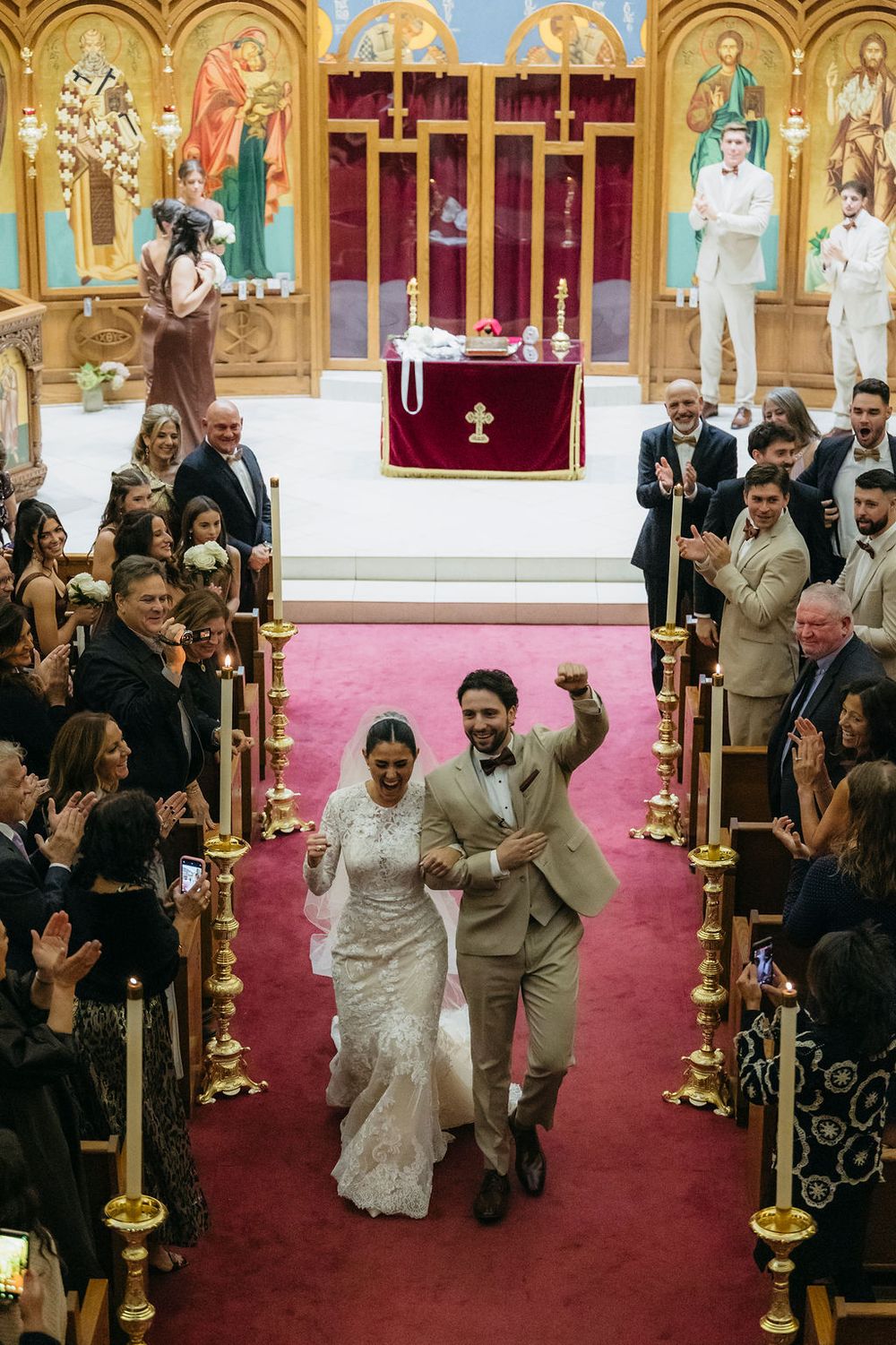 Joyful newlyweds celebrate walking down the aisle in an ornate Orthodox church, surrounded by cheering guests in Chicago