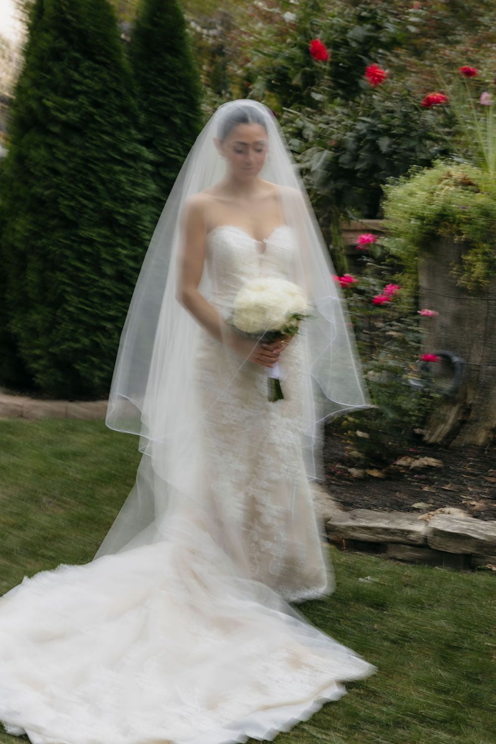 Elegant bride in strapless lace gown and veil holds white bouquet in a lush garden setting at Meson Sabika venue in Naperville, IL