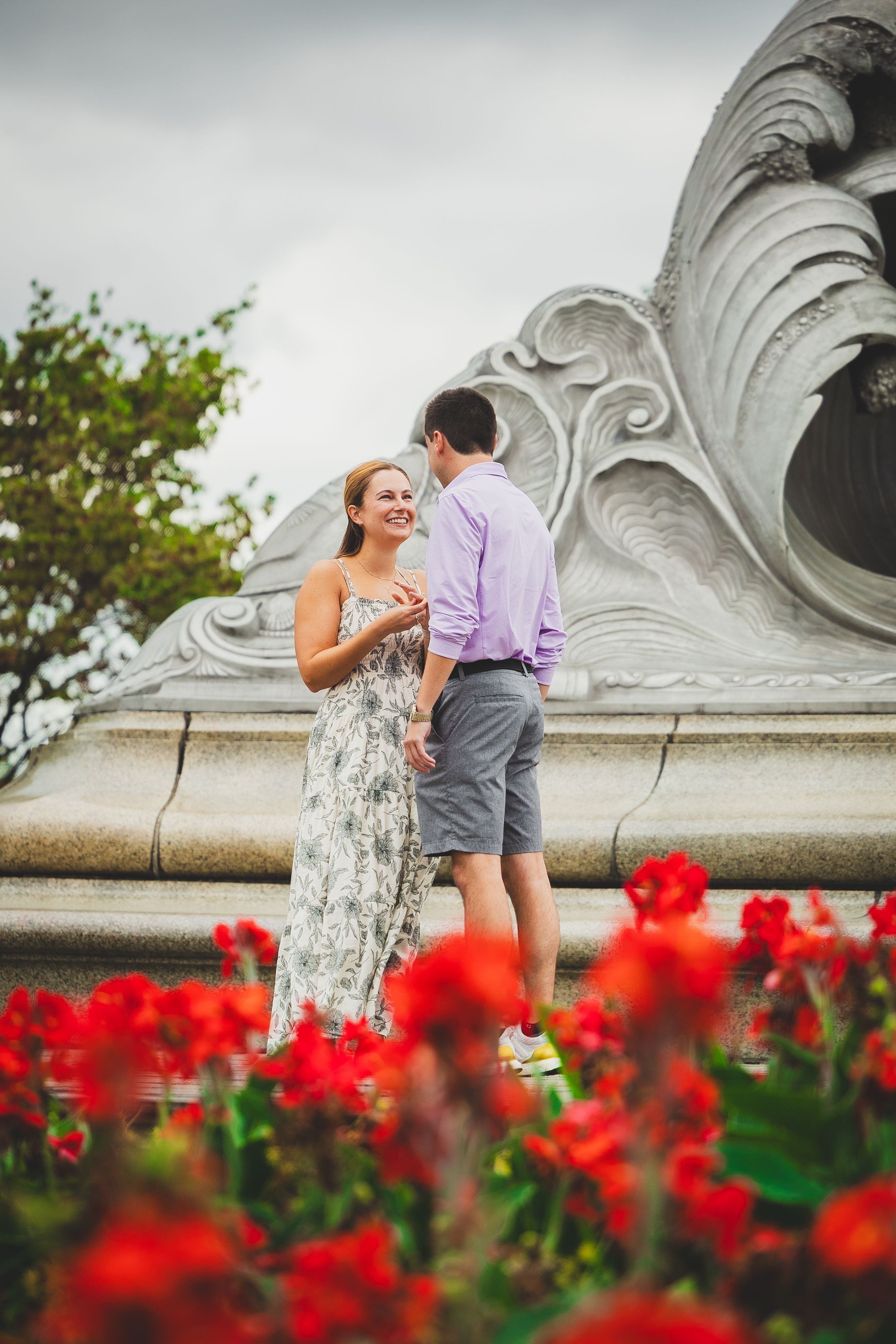 Couple sharing a romantic moment near an ornate fountain with vibrant red flowers in the foreground.