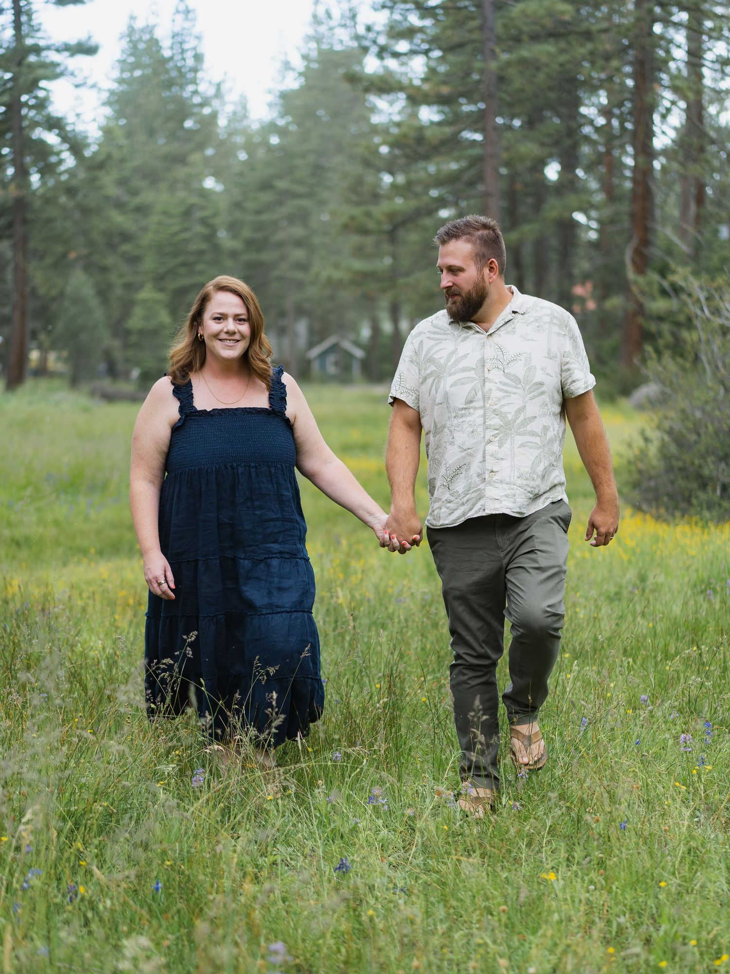 Smiling couple walking hand in hand through lush green wildflower meadow.