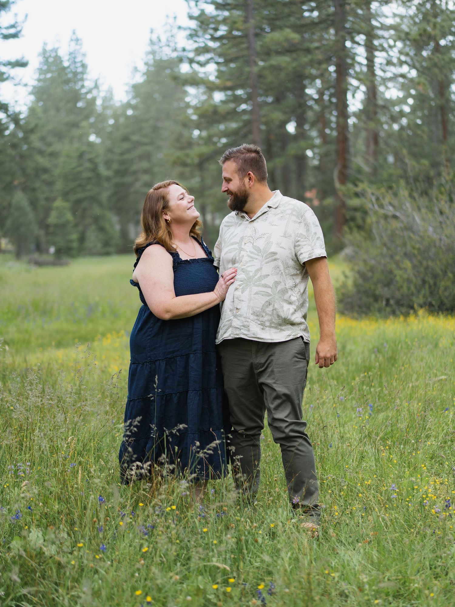 Couple sharing a tender moment in a wildflower meadow surrounded by tall pine trees.