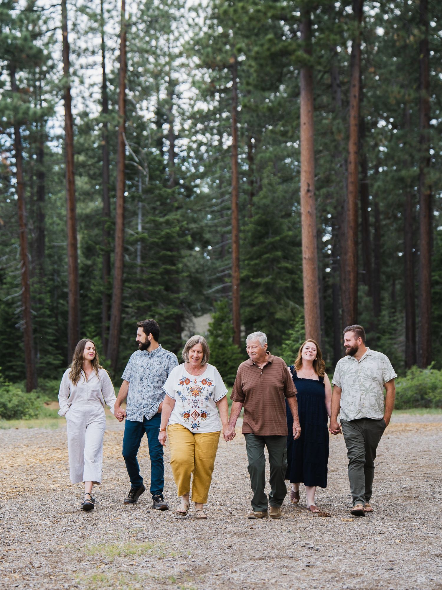 Family of six walking together on a forest path among tall pine trees.