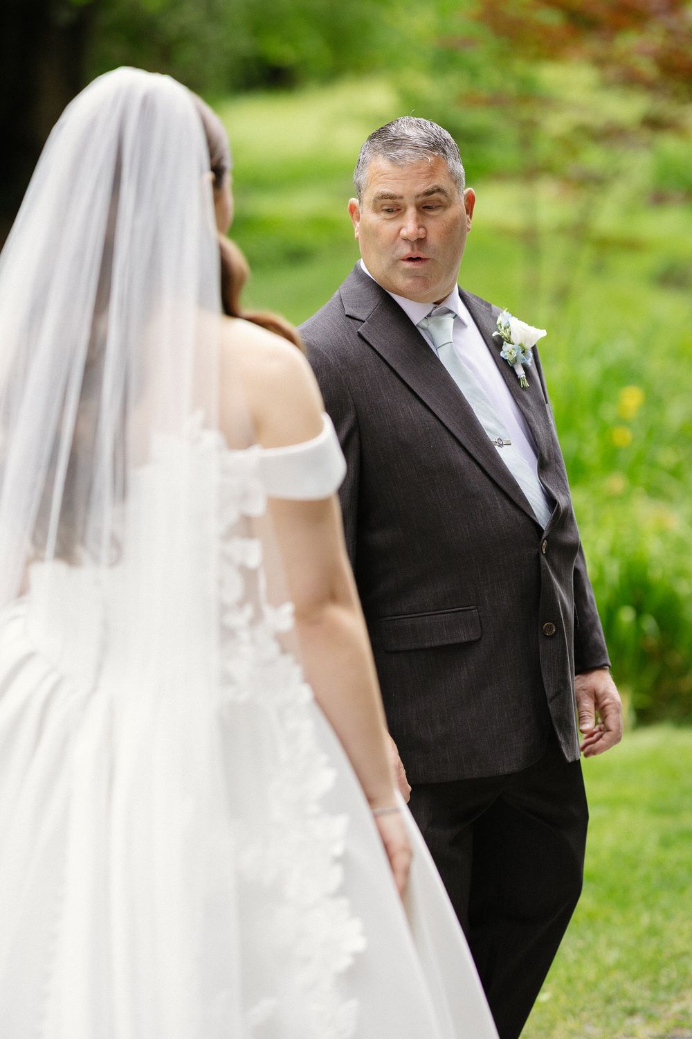 Father sees bride in wedding dress for first look moment outdoors.