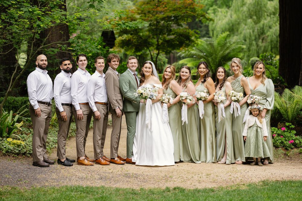 Wedding party poses in garden with sage green bridesmaids dresses.