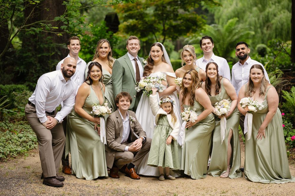 Bride and groom with wedding party in sage green dresses posing in garden.