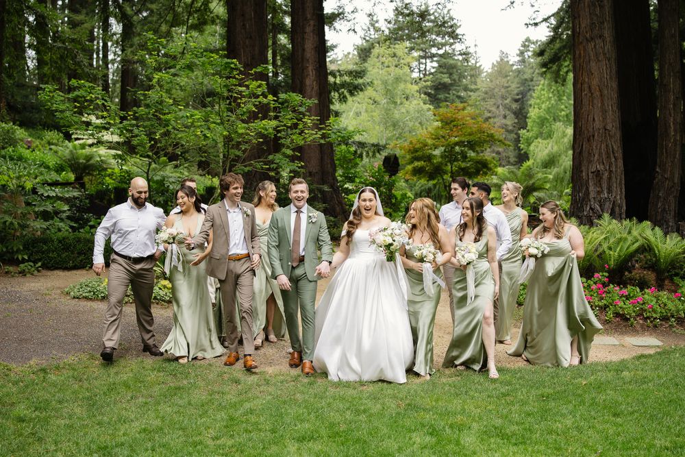 Wedding party walking through redwood garden, bridesmaids in sage green dresses alongside groomsmen in tan suits.