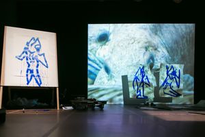 Blue figure drawings on easel beside sculptural cutouts with large projected ocean creature image on stage.