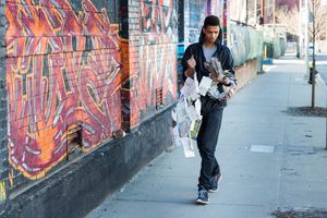 Person walking on urban sidewalk past colorful graffiti wall, carrying newspapers in city street setting.